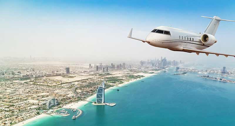 Business jet airplane flying over Dubai city and sea coastline